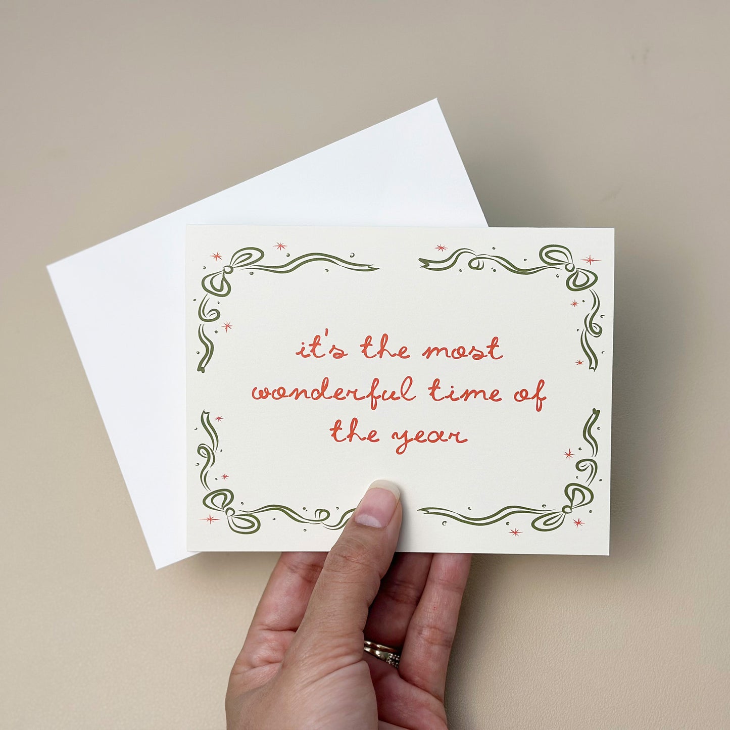 A beautifully illustrated holiday card with the phrase "It's the Most Wonderful Time of the Year," surrounded by an elegant green and red decorative border. The card includes a white envelope, ideal for spreading holiday joy and warm wishes.