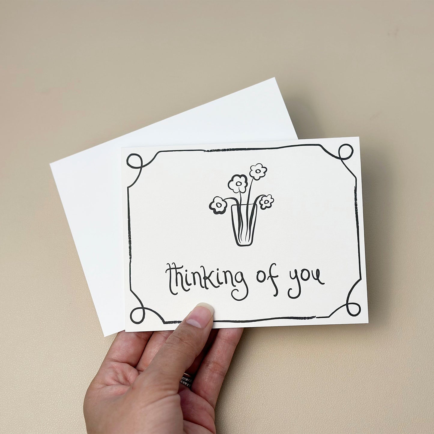 A hand-drawn "thinking of you" card featuring a vase with whimsical flowers and a decorative border. The card has an elegant, minimalist design and includes a white envelope, perfect for sending heartfelt messages of care and support.
