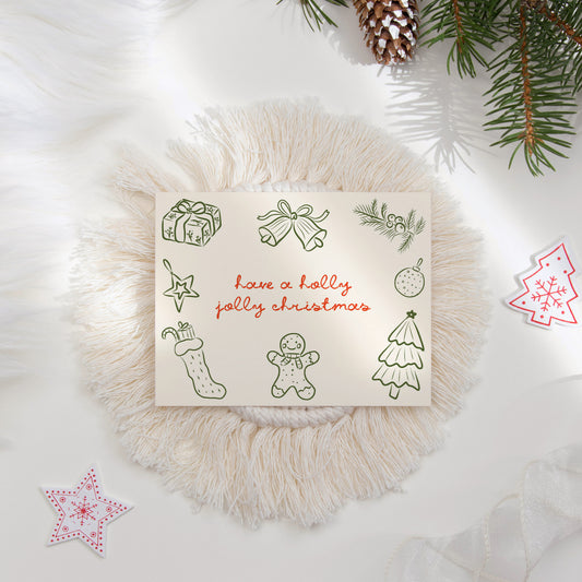 A cheerful "Holly Jolly Christmas" card featuring hand-drawn holiday illustrations such as a gingerbread man, stocking, ornaments, gifts, and a Christmas tree. The card includes whimsical green and red accents and is surrounded by cozy festive decor, perfect for holiday gifting.