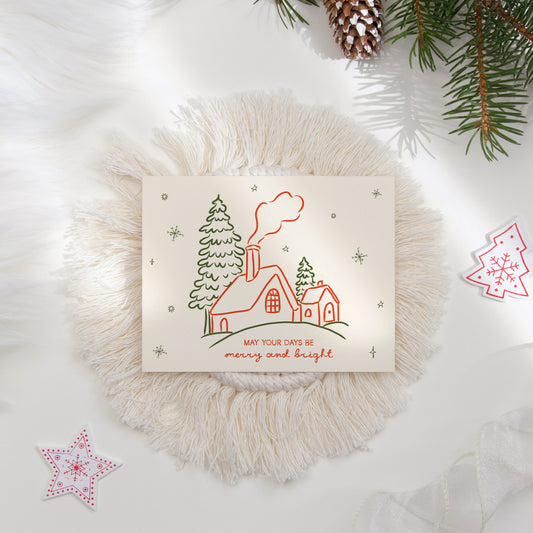 A cozy "May Your Days Be Merry and Bright" holiday card featuring hand-drawn illustrations of a snowy cottage, pine trees, and snowflakes. Styled with red and green accents and surrounded by festive decor, perfect for spreading seasonal cheer.