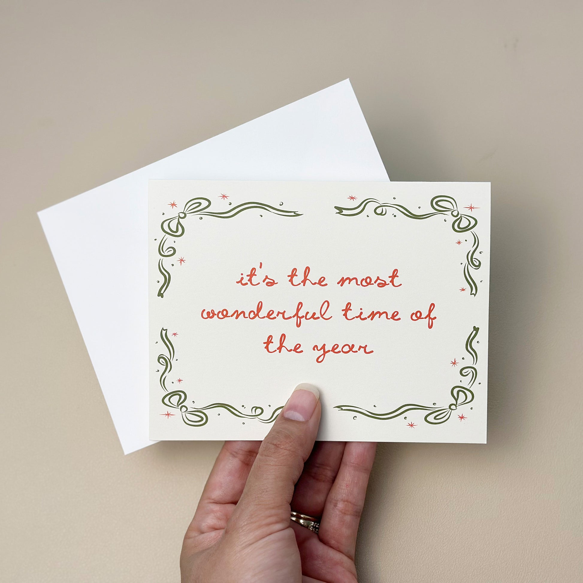 A beautifully illustrated holiday card with the phrase "It's the Most Wonderful Time of the Year," surrounded by an elegant green and red decorative border. The card includes a white envelope, ideal for spreading holiday joy and warm wishes.